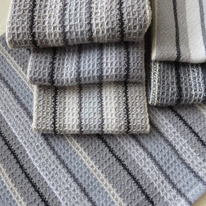 May include: A stack of four gray and white striped kitchen towels with a waffle weave texture.