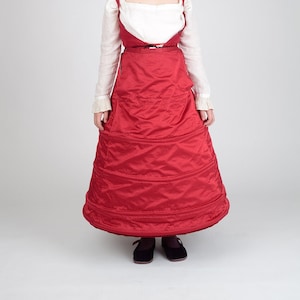 Peut inclure: Une jeune personne portant une blouse blanche avec une jupe rouge à plusieurs couches. La jupe a une forme large et circulaire et est froncée à la taille.