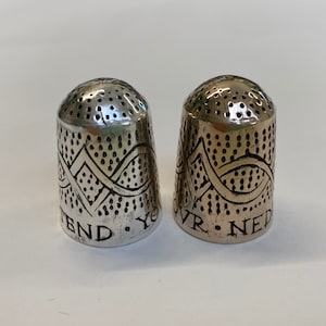 May include: Two silver thimbles with a decorative design and the words "Attend Your" and "Over Ned" engraved on the bottom.