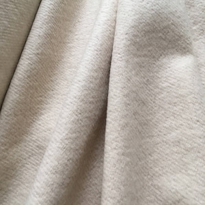 May include: Close-up of a white, textured fabric with a soft, fuzzy appearance. The fabric is folded and draped, creating a smooth, flowing texture.