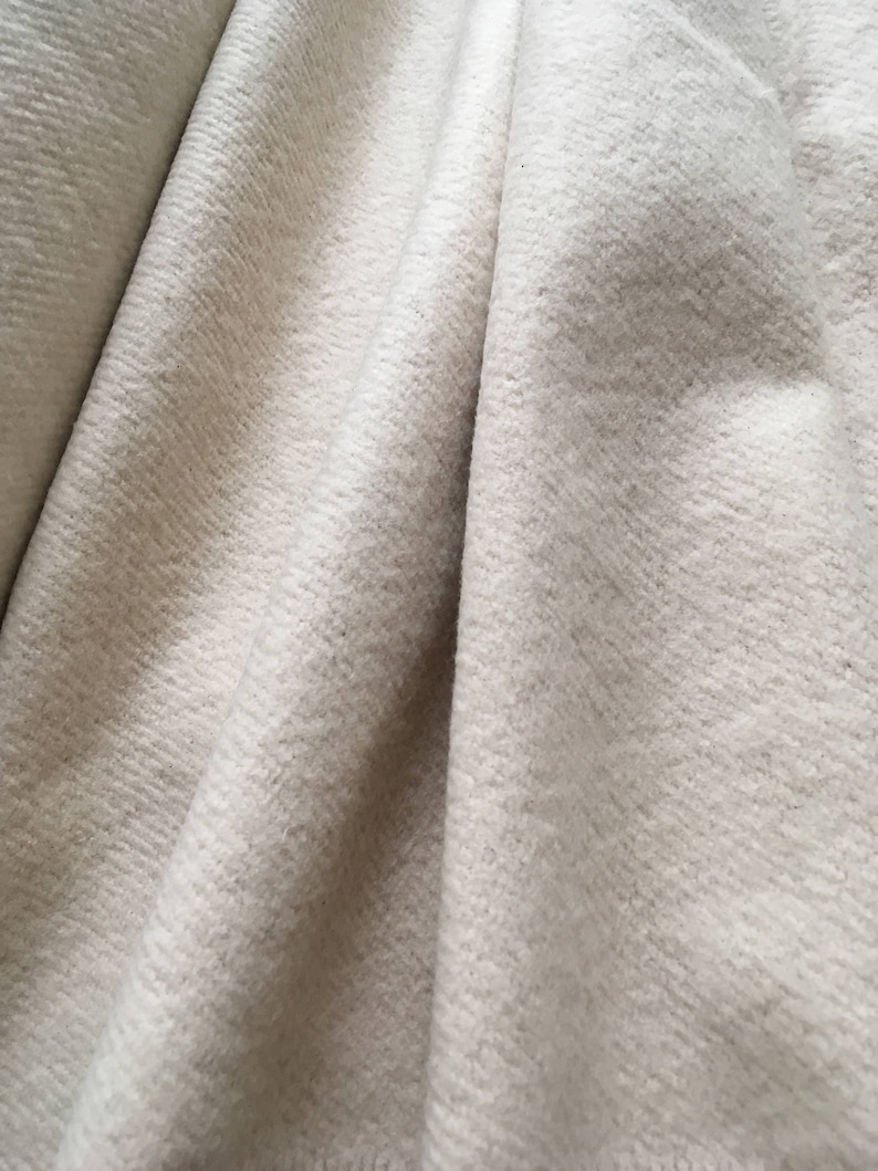 Puede incluir: Primer plano de una tela blanca texturizada con un aspecto suave y peludo. La tela est&aacute; doblada y drapeada, creando una textura suave y fluida.