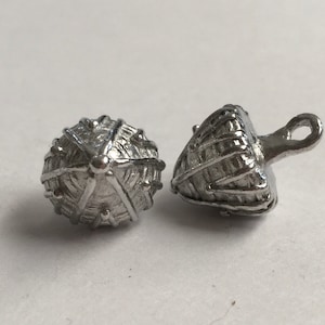 May include: Two silver metal buttons with intricate designs. One button is round and the other is a cone shape with a loop.