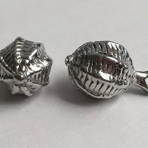 Könnte beinhalten: Zwei silberne Metallperlen mit einem strukturierten Design. Eine Perle ist rund und die andere ist oval mit einer Schlaufe an der Seite.