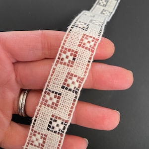 May include: White cotton lace trim with a black geometric pattern. The lace is approximately 1 inch wide.
