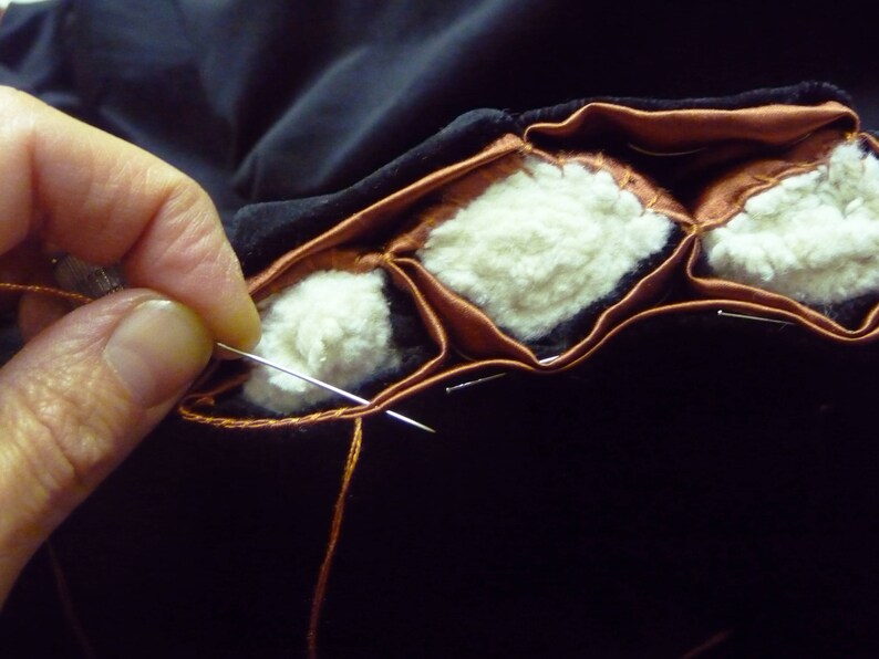 Puede incluir: Primer plano de una mano cosiendo un coj&iacute;n de tela marr&oacute;n y blanco. El coj&iacute;n est&aacute; hecho de varias capas de tela y se est&aacute; cosiendo con una aguja e hilo.