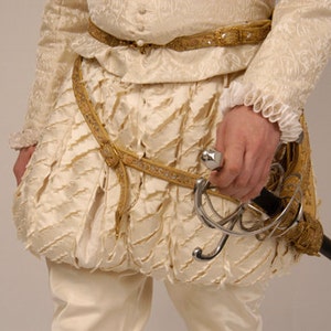 May include: A white, ruffled, and gathered fabric garment with a gold belt and a silver sword attached to it.