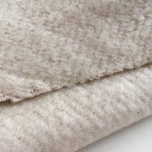 Puede incluir: Primer plano de una tela beige texturizada doblada por la mitad. La tela tiene una textura suave y peluda y parece estar hecha de fibras naturales.