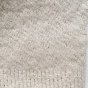 Puede incluir: Primer plano de una tela blanca de punto con un patr&oacute;n de espiga texturizado. La tela tiene una textura suave y peluda y un borde ligeramente deshilachado.