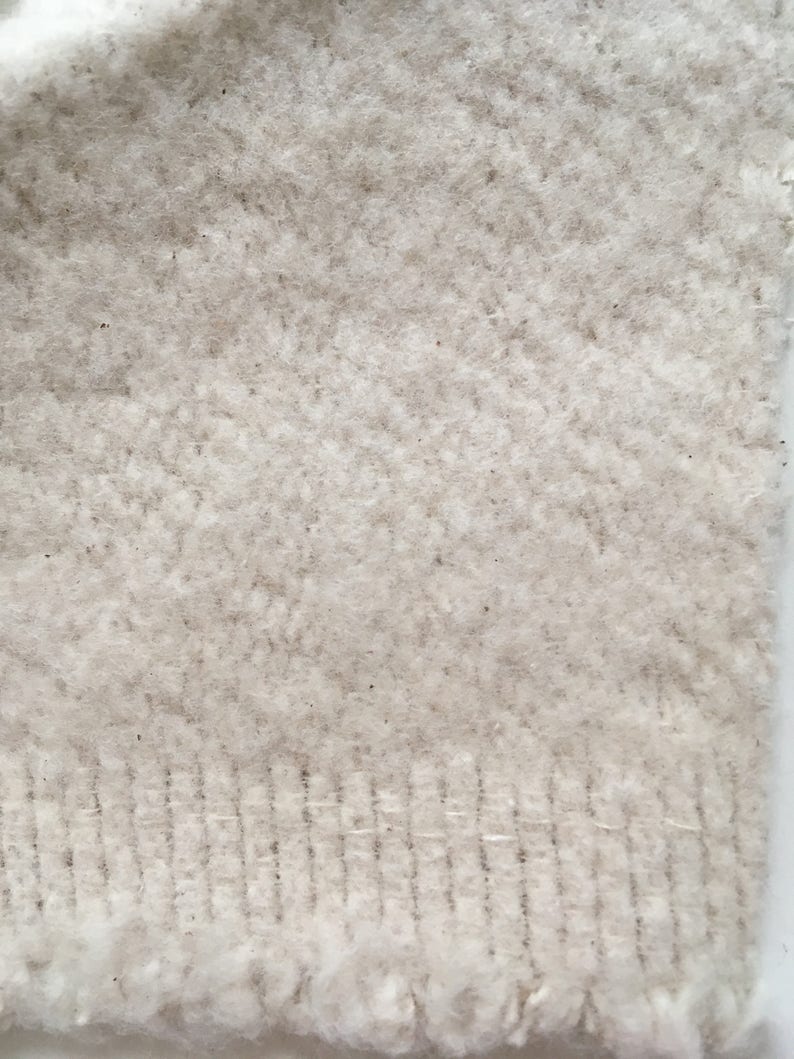 Puede incluir: Primer plano de una tela blanca de punto con un patr&oacute;n de espiga texturizado. La tela tiene una textura suave y peluda y un borde ligeramente deshilachado.