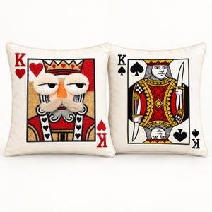 May include: Two square throw pillows featuring playing card designs. The left pillow shows a King of Hearts with a textured, fuzzy face and mustache. The right pillow displays a King of Spades with a printed illustration of a royal figure holding a sword.