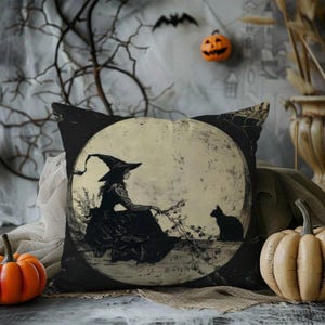 May include: A square throw pillow featuring a black and cream illustration of a witch in a pointed hat sitting before a large full moon, with a black cat facing her. The design is set against a dark background, creating a high-contrast scene.