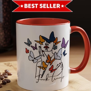 May include: White ceramic mug with a red interior and handle. The mug features a line drawing of a woman's face with butterflies and the text "Fuck Trump". A "Best Seller" banner is at the top.