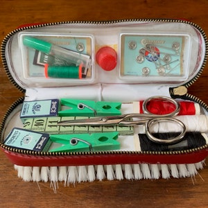 May include: A red leather sewing kit with a brush on the bottom. The kit contains a variety of sewing supplies, including needles, thread, scissors, and buttons. The kit also includes a small ruler and a few safety pins.