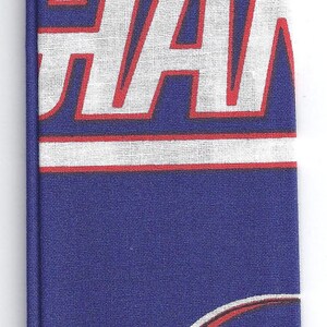 May include: A blue fabric tie featuring the word "GIANTS" in white with red trim, and a repeating pattern of football helmets. The helmets are white with black and gray details, and a red stripe.