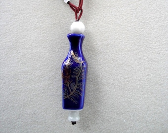 May include: A blue and gold ceramic pendant shaped like a vase hangs from a brown cord with green and red beads.
