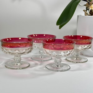 May include: Set of four clear glass dessert dishes with a red base. The dishes have a scalloped rim and a clear glass stem.