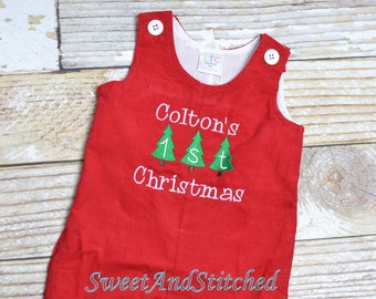 May include: Red corduroy baby overalls with white embroidery that reads "Colton's 1st Christmas" with three green Christmas trees. The overalls have two white buttons on the straps.