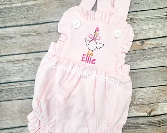 May include: Pink baby romper with a ruffle trim and embroidered goose with a pink bow and the name "Ellie".