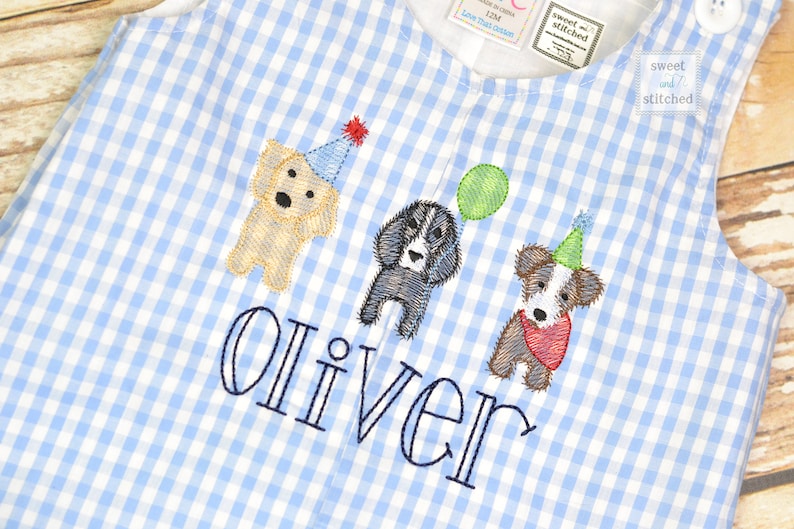 May include: Blue and white gingham fabric baby onesie with embroidered dogs wearing party hats and the name "Oliver" in blue thread.