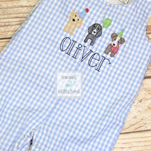 May include: Blue and white gingham overalls with embroidered dogs wearing party hats and the name "Oliver" and the text "sweet and stitched".