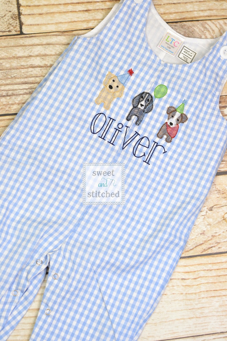 May include: Blue and white gingham overalls with embroidered dogs wearing party hats and the name "Oliver" and the text "sweet and stitched".