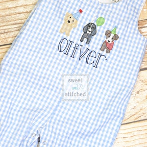 May include: Blue and white gingham baby overalls with embroidered dogs and the name "Oliver" in black thread. The overalls have a small label that says "sweet and stitched".