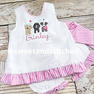 Puede incluir: Conjunto de beb&eacute; de seersucker blanco con ribete y volantes a rayas rosas. La parte superior presenta un dise&ntilde;o bordado de tres perros con sombreros de fiesta y el nombre "Brinley". El conjunto incluye una diadema y bragas a juego.