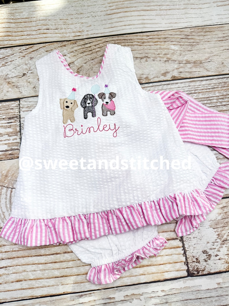 Puede incluir: Conjunto de beb&eacute; de seersucker blanco con ribete y volantes a rayas rosas. La parte superior presenta un dise&ntilde;o bordado de tres perros con sombreros de fiesta y el nombre "Brinley". El conjunto incluye una diadema y bragas a juego.
