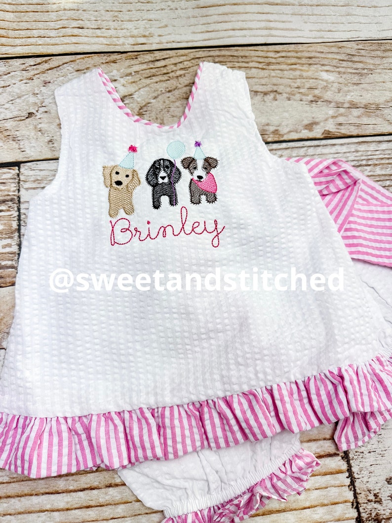 Puede incluir: Conjunto de beb&eacute; de seersucker blanco con ribete y volantes a rayas rosas. La parte superior sin mangas presenta perros bordados con sombreros de fiesta y globos, con el nombre "Brinley" bordado debajo. El conjunto incluye bragas a juego.
