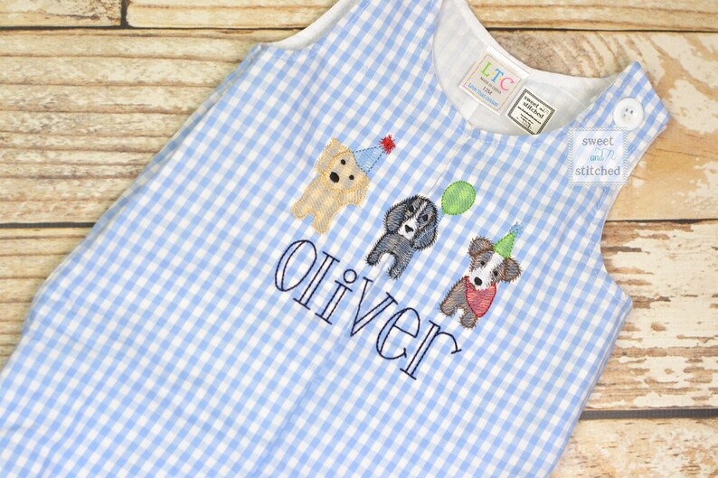 May include: A blue and white gingham baby onesie with a personalized name "Oliver" embroidered on the front. Three embroidered dogs are wearing party hats and one is holding a balloon. The onesie has a small tag that says "sweet & stitched".