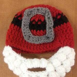 Peut inclure: Un bonnet de Noël en crochet rouge et blanc avec une ceinture en crochet noir et gris et une barbe en crochet blanc.