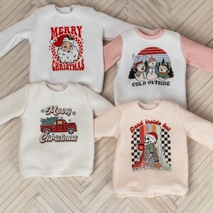 Puede incluir: Cuatro camisas de manga larga de color crema con diseños navideños. Las camisas presentan a Papá Noel, muñecos de nieve, un camión con un árbol de Navidad y un esqueleto con el texto "Dead inside but it's Christmas".