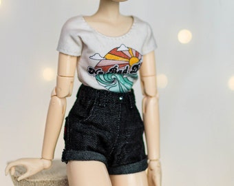 May include: A doll with red curly hair in pigtails wearing a white t-shirt with a graphic of a sunset and waves and the text "No Bad Days" and black denim shorts.