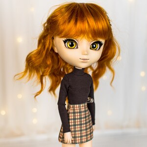 May include: A doll with long, curly, auburn hair, wearing a black turtleneck sweater and a plaid skirt. The doll has large, yellow eyes and a neutral expression.