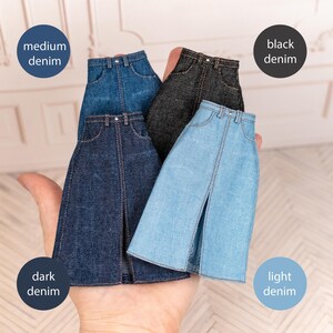 May include: Four miniature denim skirts in various shades: medium, black, dark, and light denim. Each skirt has a front slit and classic jean pocket details. The skirts are held in a hand, showcasing the different colors.