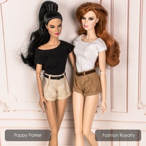 May include: Two fashion dolls wearing casual outfits. The doll on the left is wearing a black short-sleeved shirt, a beige pair of shorts, and a black belt. The doll on the right is wearing a white short-sleeved shirt, brown shorts, and a brown belt. The dolls are standing on a white background with a decorative pattern.