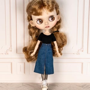 May include: A doll with long, wavy auburn hair styled in pigtails. The doll wears a black short-sleeved top and a denim skirt with a front slit. The doll's outfit is completed with white shoes and fishnet stockings.