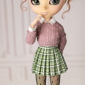 May include: A doll with large green eyes, wearing a pink sweater, a green plaid skirt, and black tights.