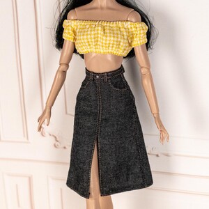 May include: A doll wearing a yellow and white gingham off-the-shoulder crop top and a dark denim skirt with a front slit. The skirt has a high waist and a visible belt loop. The outfit is designed for a doll.