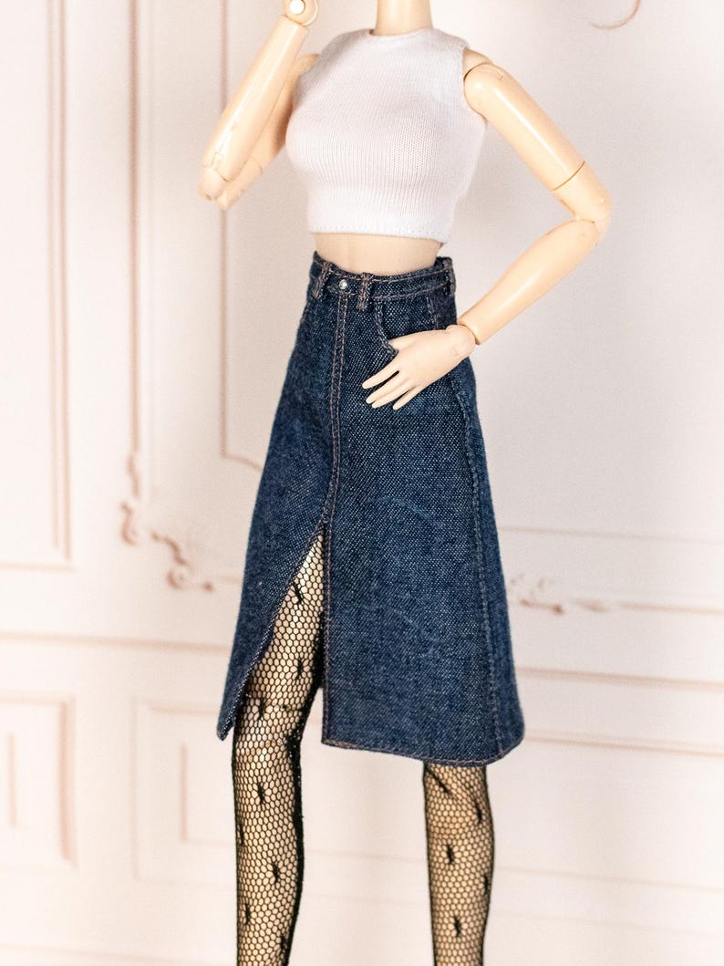 May include: A white ribbed crop top paired with a dark wash denim skirt featuring a front slit. The outfit is accessorized with black patterned tights. The doll-sized clothing is displayed against a light background.