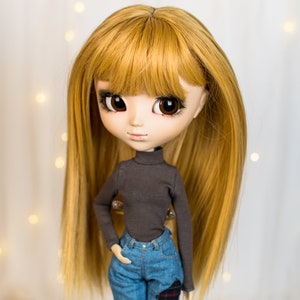 May include: A doll with long, straight, golden blonde hair, wearing a dark grey turtleneck sweater and blue jeans with a plaid patch.