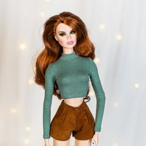 May include: A doll with long, wavy red hair wearing a green turtleneck sweater and brown corduroy shorts.