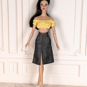 May include: A fashion doll wearing a yellow gingham crop top and a dark denim skirt with a front slit. The doll is also wearing white sneakers. The doll has long black hair and is posed in front of a white wall.