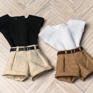 May include: Two pairs of shorts with matching tops. One pair of shorts is beige with a black belt and a black short-sleeved top. The other pair of shorts is brown with a brown belt and a white short-sleeved top.