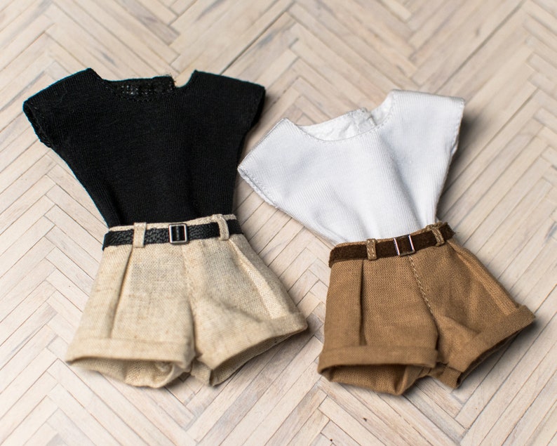 May include: Two pairs of shorts with matching tops. One pair of shorts is beige with a black belt and a black short-sleeved top. The other pair of shorts is brown with a brown belt and a white short-sleeved top.