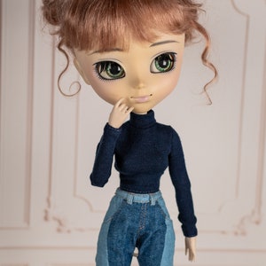 May include: A doll with brown hair styled in two buns, wearing a dark blue turtleneck sweater and blue jeans.