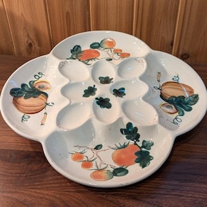 May include: White ceramic serving platter with multiple compartments, featuring hand-painted illustrations of tomatoes and pumpkins. The platter has a unique, four-lobed shape and is ideal for serving appetizers or small dishes.