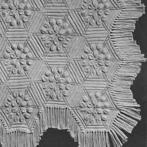 Peut inclure: Une couverture tricotée blanc cassé avec un motif floral. Le design présente des formes hexagonales avec des motifs floraux au centre. Le bord de la couverture est orné de franges. Le texte "PETAL No. 652" est visible.
