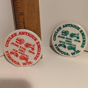 May include: Two round white buttons with red and green text. The buttons are for the Coulee Antique Engines show in Viroqua, Wisconsin. One button is for the 8th annual show in 1981 and the other is for the 10th annual show in 1983.