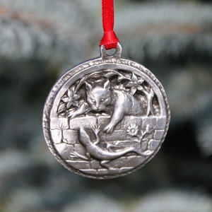 May include: A silver ornament featuring a cat and a lizard, hanging from a red ribbon.